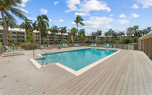 A swimming pool with a wooden deck, surrounded by palm trees and lounge chairs. - Beachfront 3br condo with pool & gym! (St. Thomas)