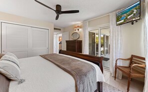 A bedroom with a bed, a wooden bench, a ceiling fan, a television, and a view of the outdoors. - Beachfront 3br condo with pool & gym! (St. Thomas)
