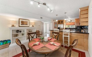A dining area with a round wooden table, four chairs, and a kitchen in the background. - Beachfront 3br condo with pool & gym! (St. Thomas)