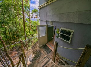 Eine Holztreppe führt zu einer Tür mit Blick auf üppiges Grün und ein Gebäude mit einem Fenster.