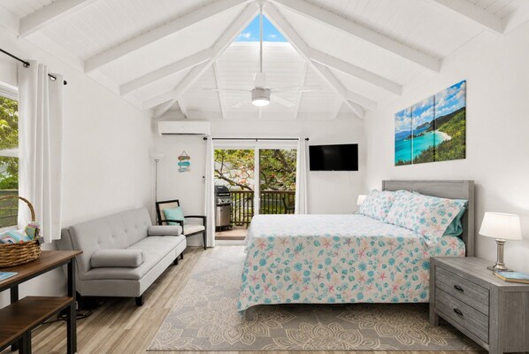 A bedroom with a bed, a TV, a sofa, a table, and a balcony with a grill.