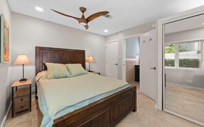 Ein Schlafzimmer mit einem hölzernen Bett, zwei Nachttischlampen, einem Deckenventilator und einer Schiebeglastür, die zu einem Außenbereich führt.