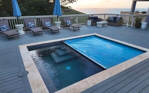 Eine Terrasse mit einem rechteckigen Whirlpool, Liegestühlen und Sonnenschirmen.