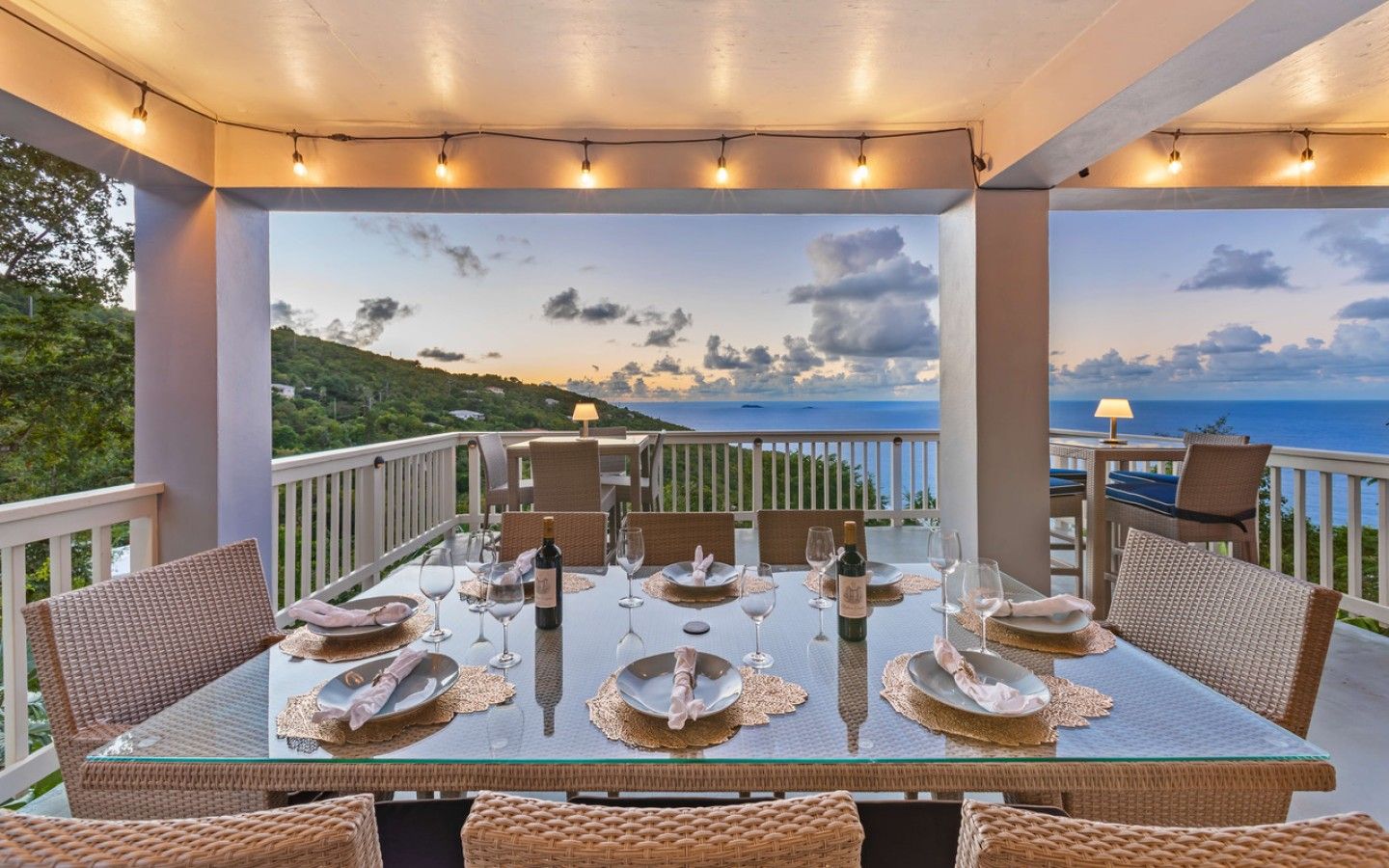A covered outdoor dining area with a table set for four, overlooking a scenic view of the sea and hills.