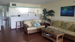 A living room with a sofa, a coffee table, a small side table, a potted plant, and a kitchen in the background. - Crystal Cove at Sapphire Beach – Sunrise Views & Steps to Paradise (St Thomas)