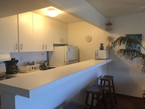 A compact kitchen with white cabinets, a refrigerator, a coffee maker, and a clock on the wall. - Crystal Cove at Sapphire Beach – Sunrise Views & Steps to Paradise (St Thomas)