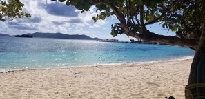 Een strand met helder water, een zandstrand en bergen in de verte.