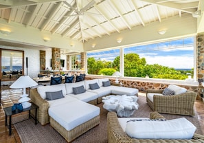 A spacious outdoor living area with a large sectional sofa, wicker furniture, and a stone wall backdrop. - Private 9BR Luxury Estate | Pool, Tennis, Views (St. Thomas)