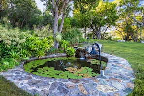 A stone pond with lily pads, surrounded by lush greenery and trees. - Private 9BR Luxury Estate | Pool, Tennis, Views (St. Thomas)