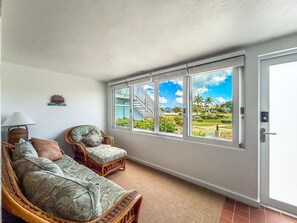 A room with a wicker sofa, two armchairs, a lamp, and a view of a golf course through large windows. - Sapphire Beachfront Condo w/ Pool, 2 Baths (St. Thomas)