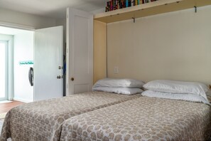 A bedroom with two beds, a door, and a bookshelf with books. - Sapphire Beachfront Condo w/ Pool, 2 Baths (St. Thomas)