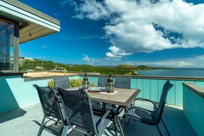 A balcony with a table and chairs, overlooking a scenic view of the sea and hills. - Budget friendly 2br condo - walk to the beach! (St. Thomas)