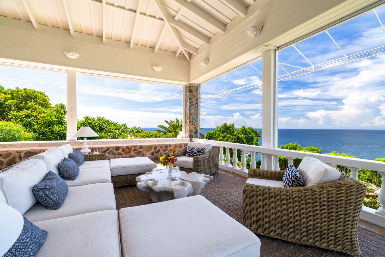 A covered outdoor seating area with a view of the ocean, furnished with sofas and a coffee table.