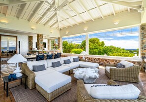 A spacious outdoor living area with a large sectional sofa, wicker furniture, and a stone wall backdrop. - Bellevue Estate- 6BR New remodel w/Restoration Hardware & Tennis (St. Thomas)