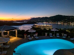 A swimming pool with lounge chairs and umbrellas, overlooking a body of water and a cityscape at dusk. - 2BR New remodel w/Restoration Hardware & Tennis (Charlotte Amalie East)