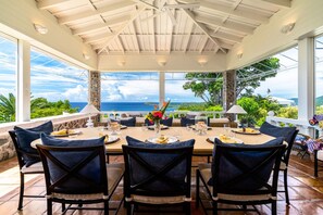 A covered outdoor dining area with a view of the ocean, furnished with tables and chairs, and a decorative centerpiece. - 2BR New remodel w/Restoration Hardware & Tennis (Charlotte Amalie East)