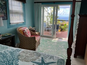 Ein Schlafzimmer mit einem Bett, einem Korbstuhl, Blick ins Freie und einem Schminktisch.