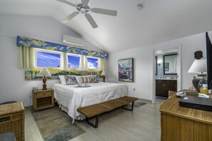 Ein Schlafzimmer mit Bett, einer Sitzbank, einem Schreibtisch, einem Deckenventilator und Blick zum Himmel durch Fenster.