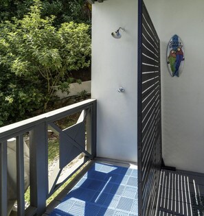 Ein Balkon mit blau gemustertem Boden, einer weißen Wand mit einem Metallgitter und einer wandmontierten Leuchte.