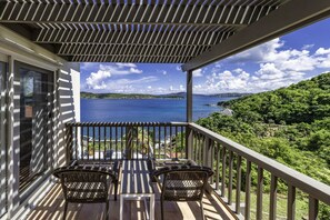 A balcony with wicker chairs and a table overlooking a lake and greenery. - Serene Luxury at Whale Watch – Your Island Oasis (St. Thomas)