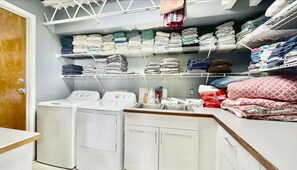 Une buanderie avec des piles de vêtements pliés rangés sur des étagères, un lave-linge et un évier.