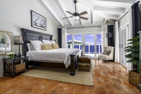 A bedroom with a large bed, a ceiling fan, a view of the sea, and a balcony with curtains. - 4BR Waterfront - 5 Minutes To Magen`s (St. Thomas)