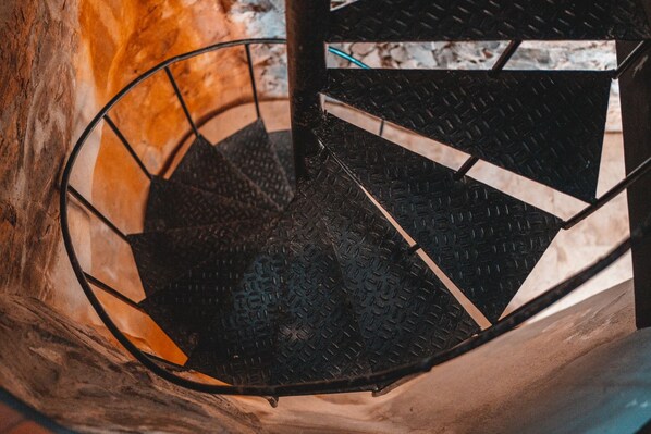 A spiral staircase with a metal railing and a textured floor. - Lissette Manor - 5BR historical estate next to The Pink Palm Hotel downtown! (St. Thomas)