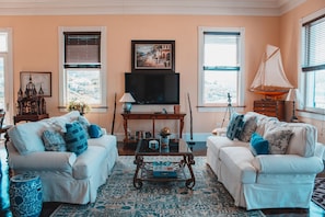 A living room with two white sofas, a coffee table, a TV, and a sailboat model. - Lissette Manor - 5BR historical estate next to The Pink Palm Hotel downtown! (St. Thomas)