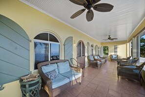 A covered patio area with wicker furniture, a ceiling fan, and large windows offering a view of the ocean. - Classic West Indies Retreat with Timeless Soul (St. Thomas)