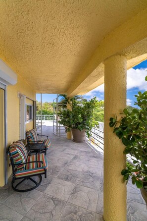A covered outdoor area with a yellow textured ceiling, two striped chairs, and potted plants. - 4BR - centrally located & mins. from Magen`s Bay! (St. Thomas)