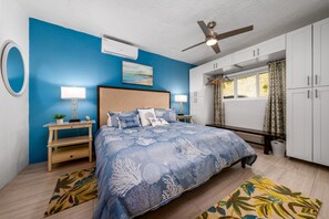 Une chambre à coucher comprenant un lit, des tables de chevet, un ventilateur de plafond, une fenêtre avec des rideaux et une vue sur l’extérieur.
