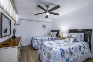 A bedroom with two beds, a ceiling fan, a nightstand with a lamp, and a dresser. - Turquoise Dreams- 2br Condo- pool, restaurant and beach! (St. Thomas)