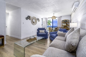 A living room with a sofa, armchairs, a glass coffee table, and a view of the ocean. - Turquoise Dreams- 2br Condo- pool, restaurant and beach! (St. Thomas)