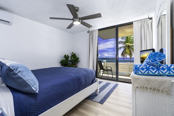 A bedroom with a bed, a ceiling fan, a view of the beach, a chair, and a TV. - Turquoise Dreams- 2br Condo- pool, restaurant and beach! (St. Thomas)