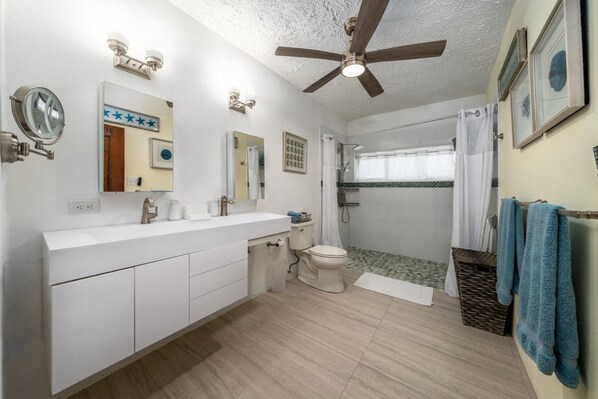 A modern bathroom with a white vanity, a ceiling fan, a shower with a glass door, and a toilet. - Centrally located 3br with pool, incredible harbor views! (St. Thomas)