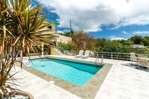 Ein Schwimmbecken mit gefliestem Deck, Liegestühlen und einer Treppe, die zu einem Gebäude führt.