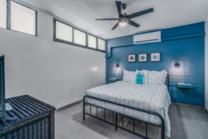 Ein Schlafzimmer mit einem Bett, Deckenventilator, Fenster und einer Wand-Klimaanlage.