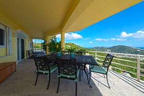 An outdoor patio with a table and chairs, potted plants, and a view of a mountainous landscape. - Centrally located 7br with pool, 3 kitchens, pool and lots of space! (St. Thomas)