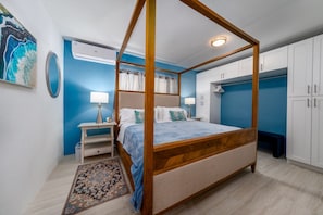 A four-poster bed with a wooden frame, a bedside table with a lamp, a wall-mounted air conditioner, and a large wardrobe with white doors. - Centrally located 7br with pool, 3 kitchens, pool and lots of space! (St. Thomas)