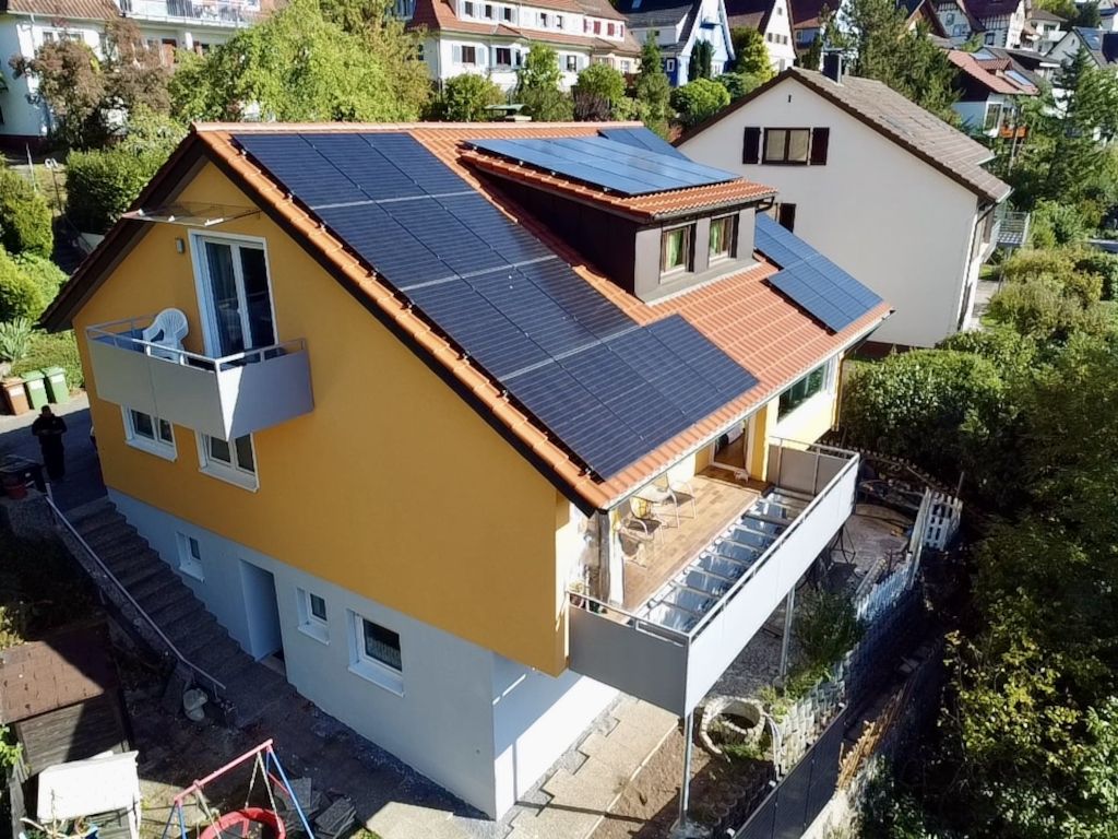 A residential building with a sloped roof, solar panels, a balcony, and a visible staircase leading to an upper level.