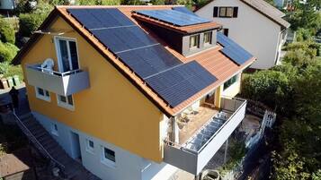 A residential building with a sloped roof, solar panels, a balcony, and a visible staircase leading to an upper level.