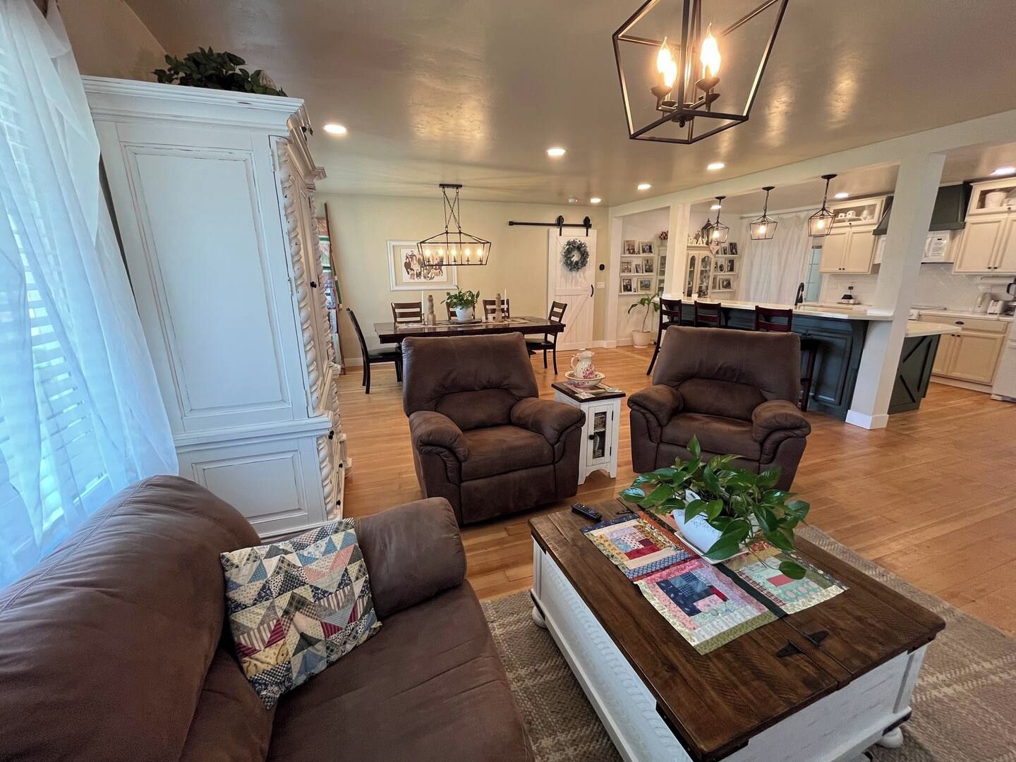 A living room with a brown sofa, a coffee table with magazines, and a dining area in the background.