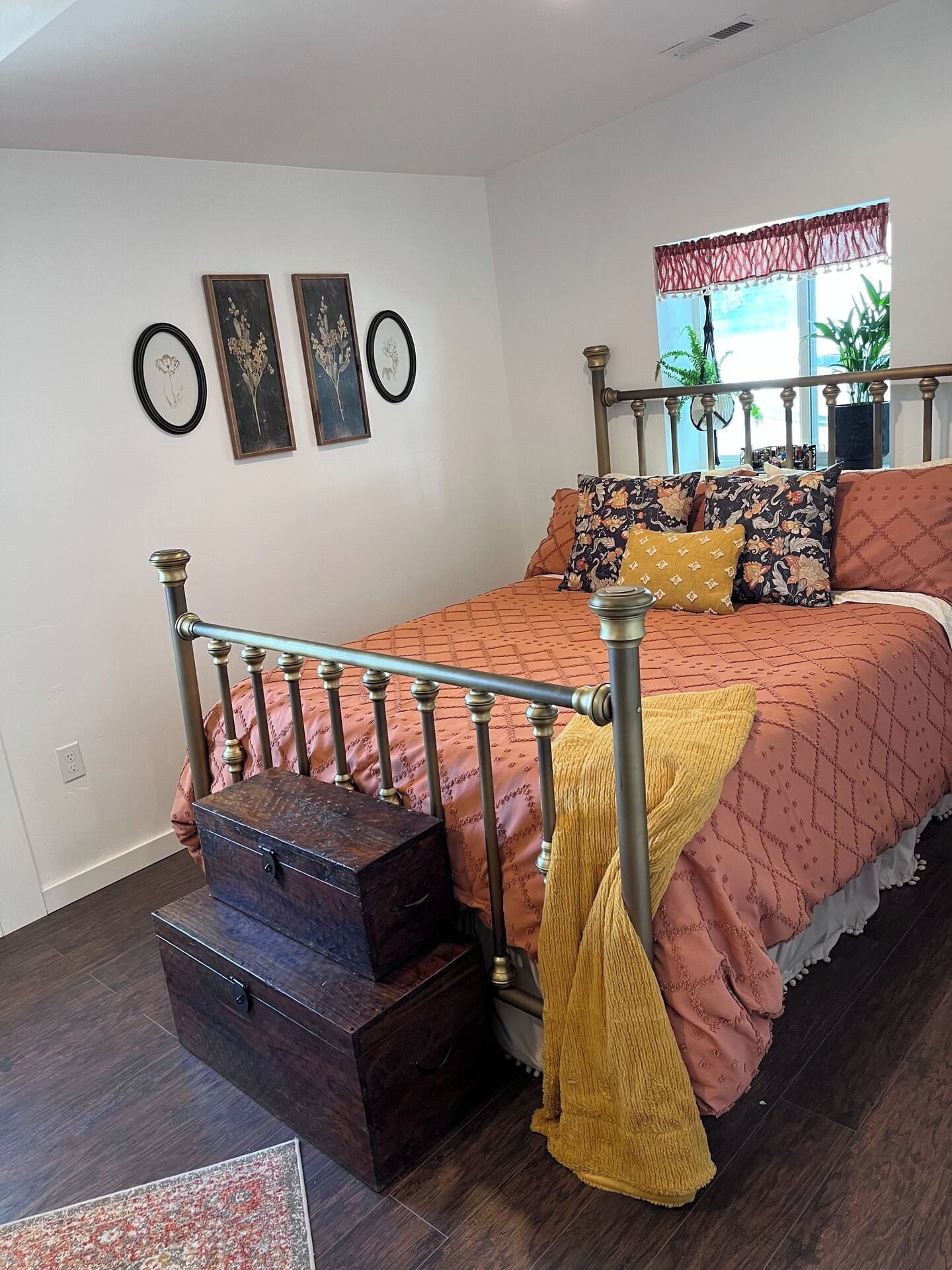 A bedroom with a bed, a chest of drawers, a window with curtains, and wall-mounted artwork.