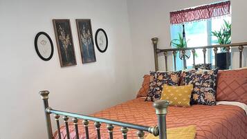A bedroom with a bed, a chest of drawers, a window with curtains, and wall-mounted artwork.