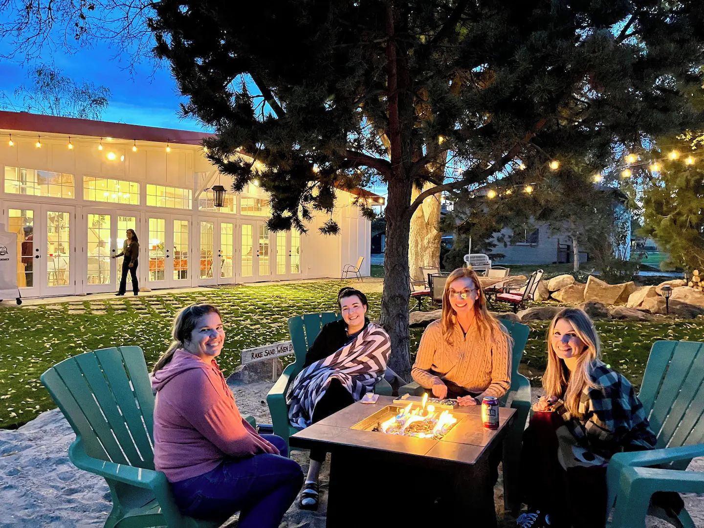 Un grupo de personas sentadas alrededor de una mesa con fuego, al aire libre al atardecer.