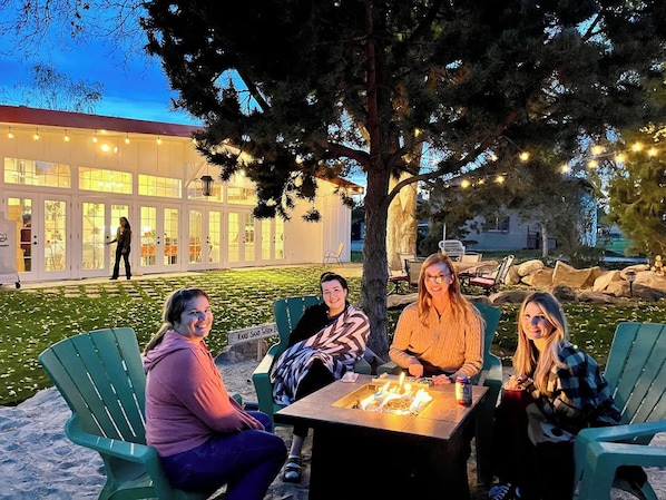 A group of people seated around a table with a fire, outdoors at dusk. - 12 BDR ID Retreat, Hot Tub, beds for 37+, Events (Nampa)