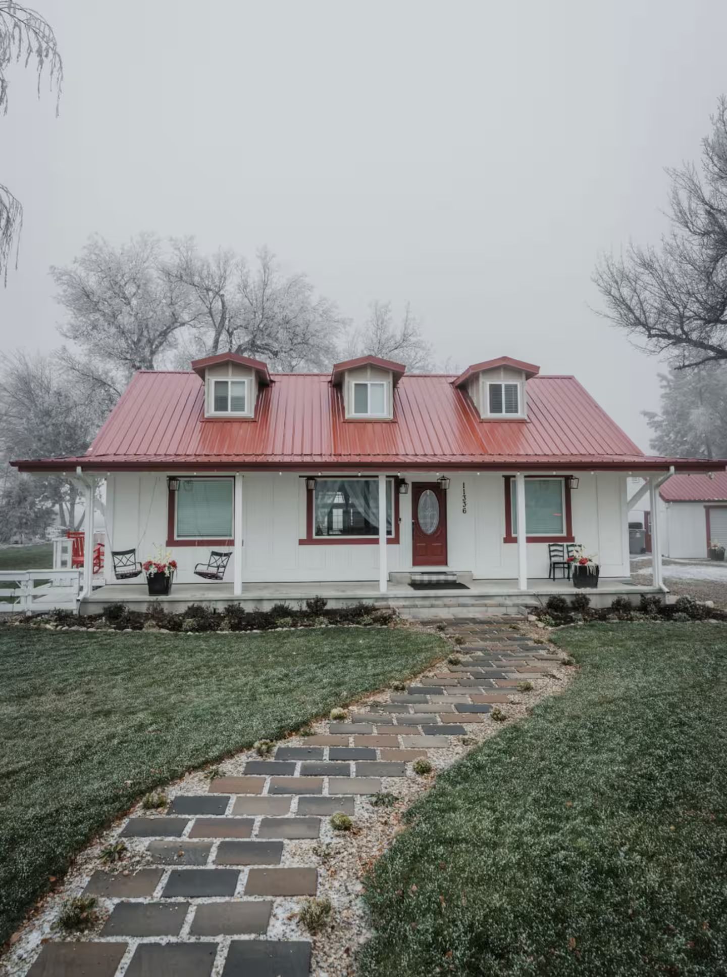 Een twee verdiepingen tellend huis met een rood dak, een veranda en een pad van stenen dat naar de ingang leidt.
