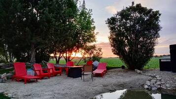 A serene outdoor seating area with red chairs and a table, surrounded by trees and a view of the sunset.
