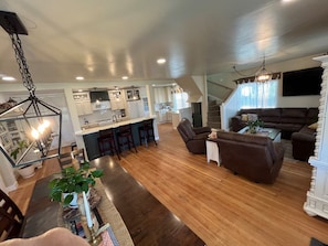 A spacious living area with a kitchen, a staircase, and a seating area with a sofa and chairs. - 12 BDR ID Retreat, Hot Tub, beds for 37+, Events (Nampa)