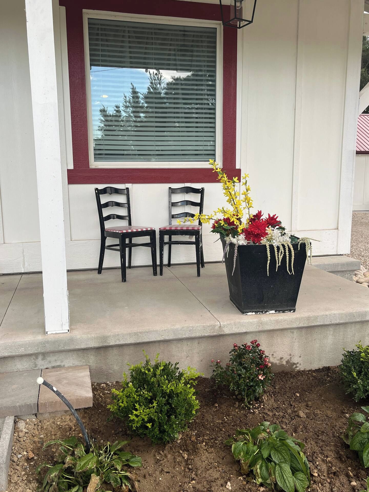Eine Veranda mit zwei Stühlen, einem Blumentopf mit Blumen und einem Fenster mit Jalousien.